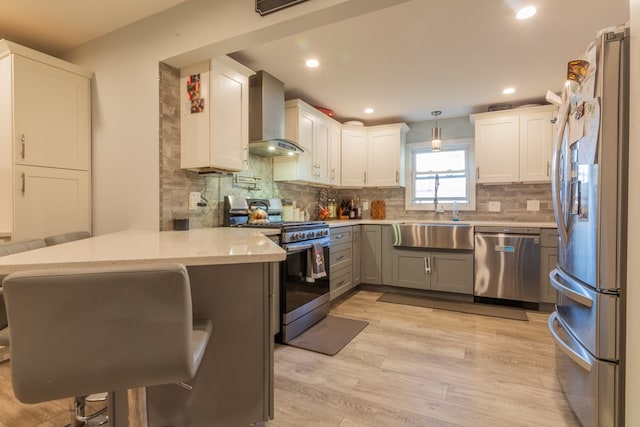 kitchen with wall chimney exhaust hood, pendant lighting, sink, stainless steel appliances, and kitchen peninsula