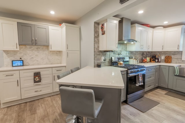 kitchen featuring wall chimney exhaust hood, a breakfast bar, stainless steel gas range oven, and white cabinetry