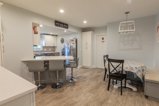 kitchen with light wood-type flooring, stainless steel appliances, a breakfast bar, pendant lighting, and white cabinetry