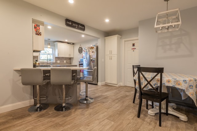 kitchen with stainless steel refrigerator, light hardwood / wood-style flooring, kitchen peninsula, white cabinets, and a kitchen bar