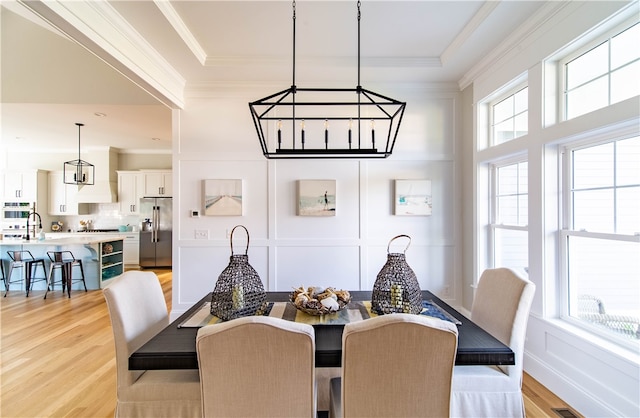 dining space featuring light hardwood / wood-style floors, crown molding, and a notable chandelier