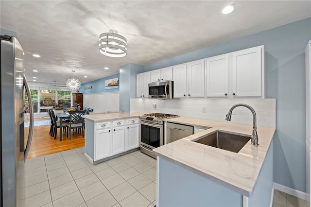 kitchen with white cabinets, sink, kitchen peninsula, hanging light fixtures, and appliances with stainless steel finishes