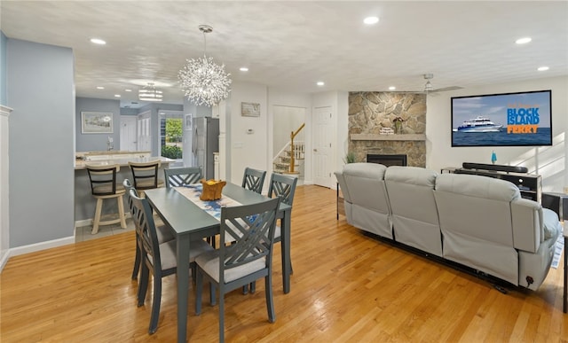 dining room with a fireplace, ceiling fan with notable chandelier, and light wood-type flooring