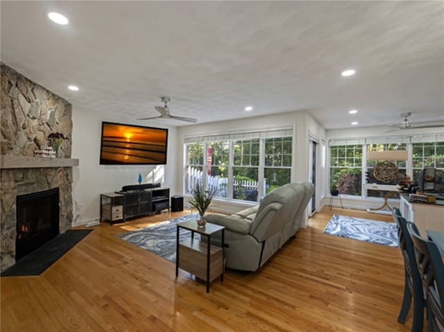 living room featuring ceiling fan, a stone fireplace, and light hardwood / wood-style floors