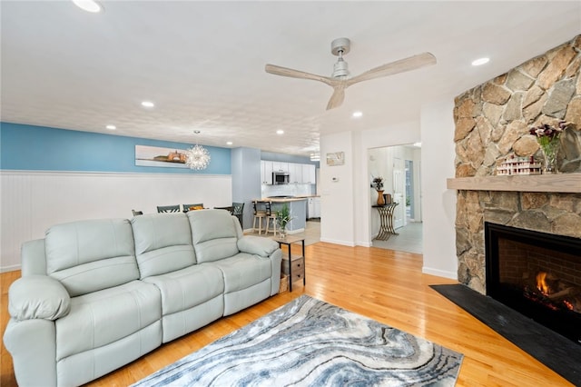 living room with a stone fireplace, light wood-type flooring, and ceiling fan