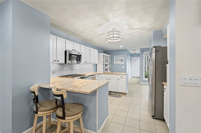 kitchen with kitchen peninsula, butcher block countertops, white cabinetry, appliances with stainless steel finishes, and a kitchen breakfast bar