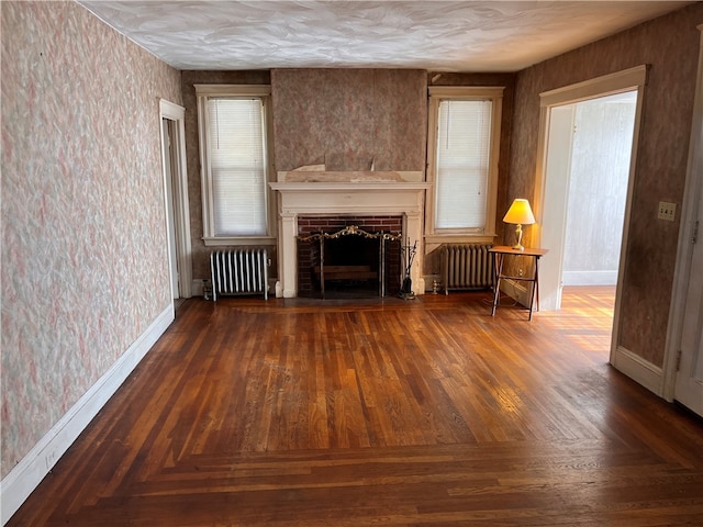 unfurnished living room with a brick fireplace, dark parquet floors, and radiator