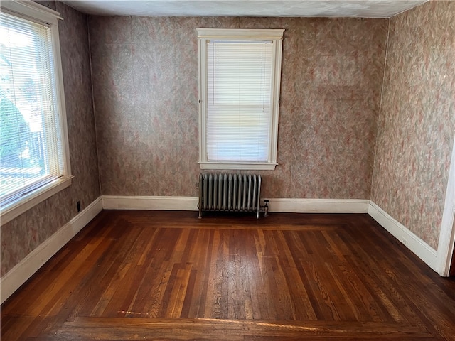 empty room featuring plenty of natural light, radiator heating unit, and dark hardwood / wood-style flooring