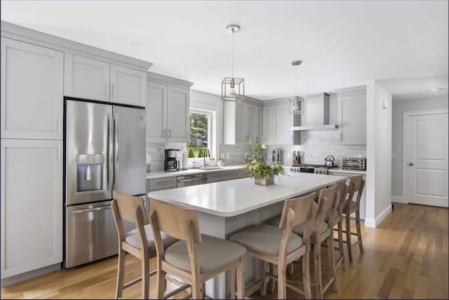 kitchen featuring a kitchen island, light wood-type flooring, decorative backsplash, stainless steel appliances, and wall chimney range hood