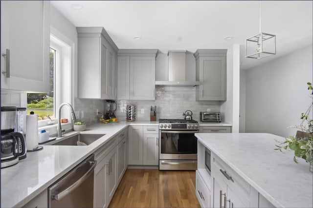 kitchen with sink, gray cabinetry, decorative light fixtures, wall chimney exhaust hood, and appliances with stainless steel finishes