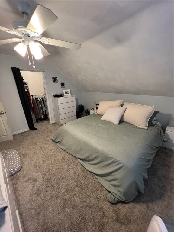 carpeted bedroom featuring a walk in closet, a closet, vaulted ceiling, and ceiling fan