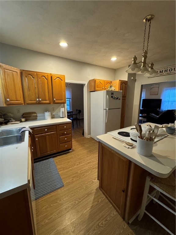 kitchen featuring sink, decorative light fixtures, white refrigerator, a chandelier, and light hardwood / wood-style floors