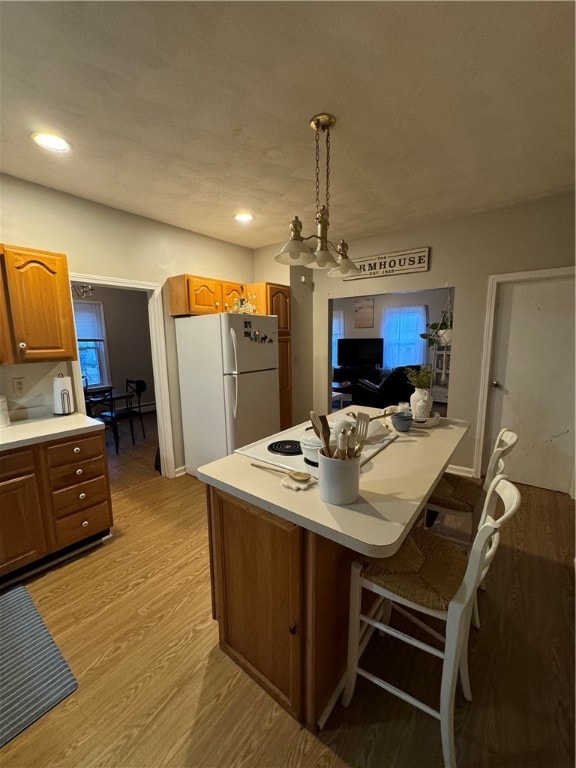 kitchen featuring a chandelier, light hardwood / wood-style floors, decorative light fixtures, a breakfast bar, and white refrigerator