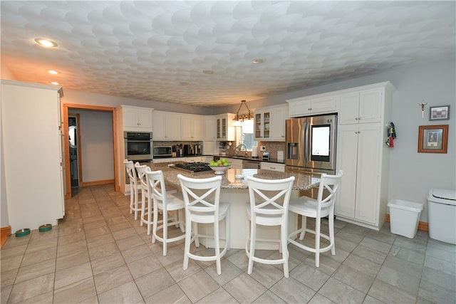 kitchen with white cabinetry, light stone counters, a kitchen island, and backsplash