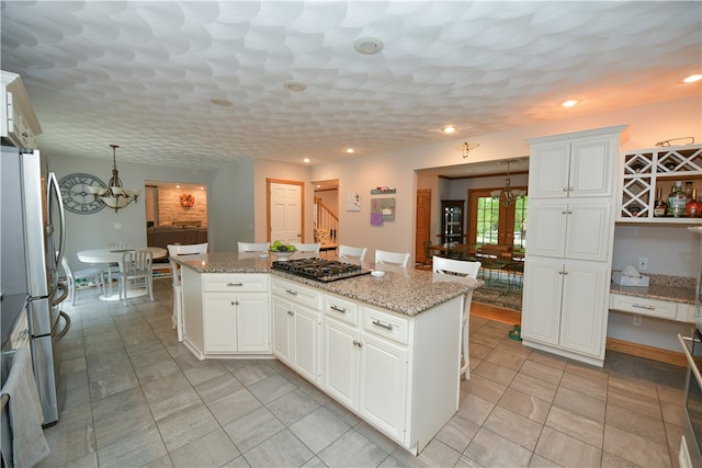 kitchen featuring light stone countertops, a center island, white cabinetry, stainless steel appliances, and an inviting chandelier