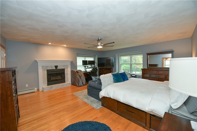 bedroom featuring light hardwood / wood-style floors, a baseboard heating unit, a premium fireplace, and ceiling fan