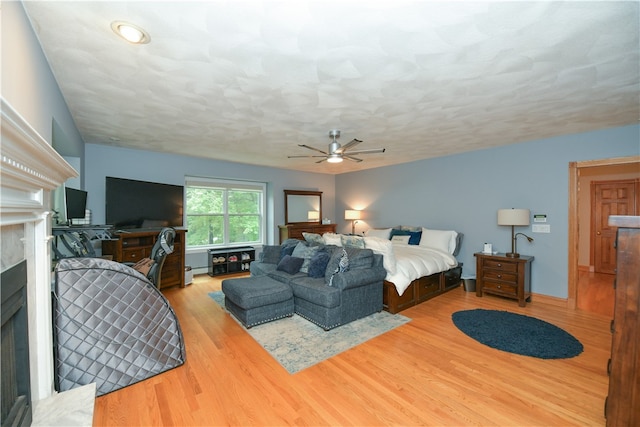 bedroom with a high end fireplace, light hardwood / wood-style floors, and ceiling fan