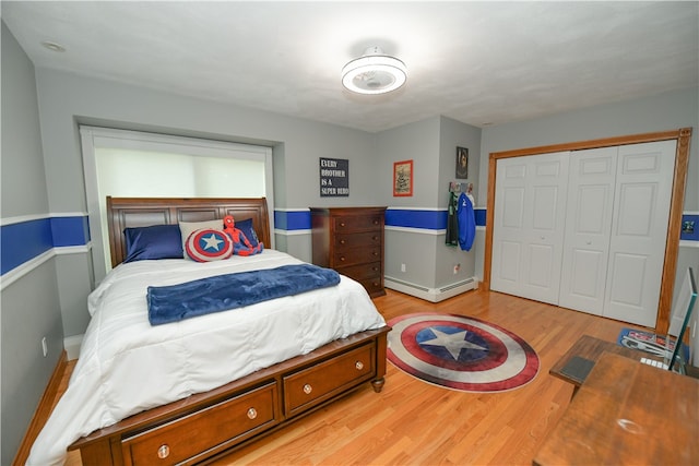 bedroom with baseboard heating, a closet, and light hardwood / wood-style floors