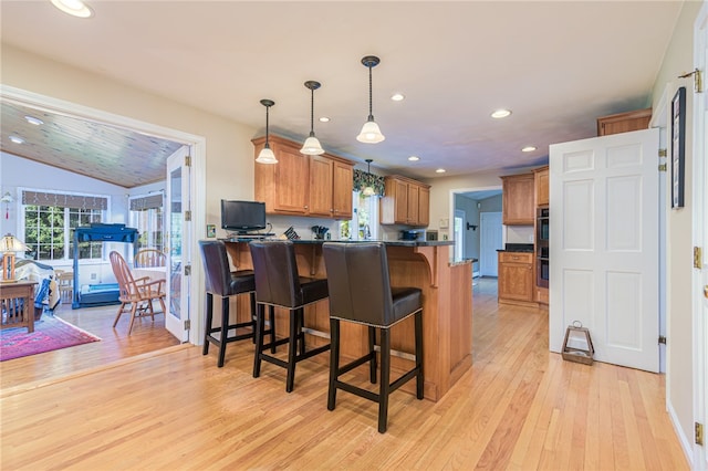 kitchen with lofted ceiling, light hardwood / wood-style floors, kitchen peninsula, hanging light fixtures, and a breakfast bar area