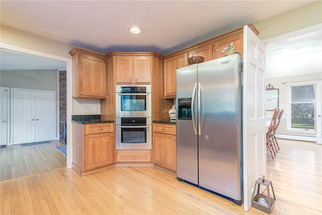 kitchen with appliances with stainless steel finishes, dark stone counters, and light wood-type flooring