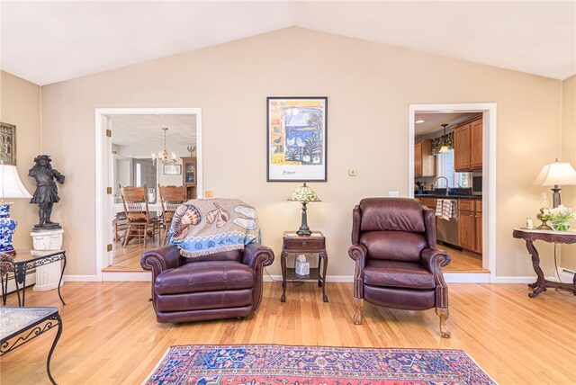 living area with vaulted ceiling, sink, a chandelier, and light hardwood / wood-style flooring