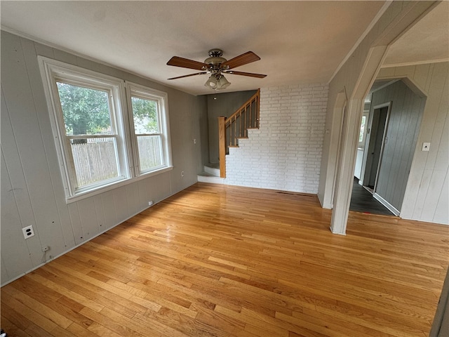 unfurnished living room featuring brick wall, ceiling fan, light wood-type flooring, and wood walls