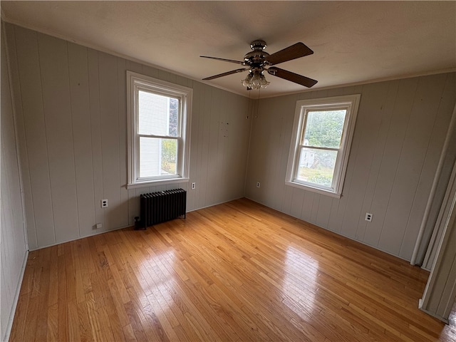 empty room with radiator, light hardwood / wood-style floors, and wood walls