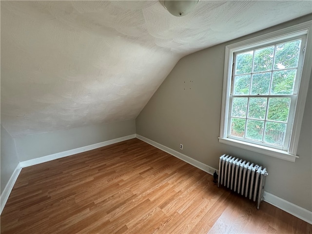 bonus room with lofted ceiling, radiator heating unit, and wood-type flooring