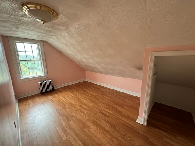 additional living space with a textured ceiling, radiator, light wood-type flooring, and vaulted ceiling