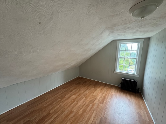 bonus room featuring lofted ceiling, a textured ceiling, radiator heating unit, and light hardwood / wood-style floors