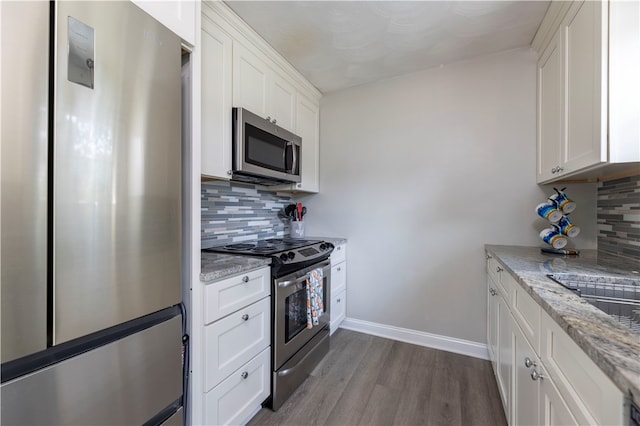 kitchen featuring decorative backsplash, white cabinetry, hardwood / wood-style flooring, light stone countertops, and stainless steel appliances