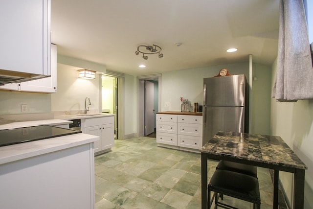 kitchen featuring black range oven, stainless steel fridge, sink, and white cabinetry