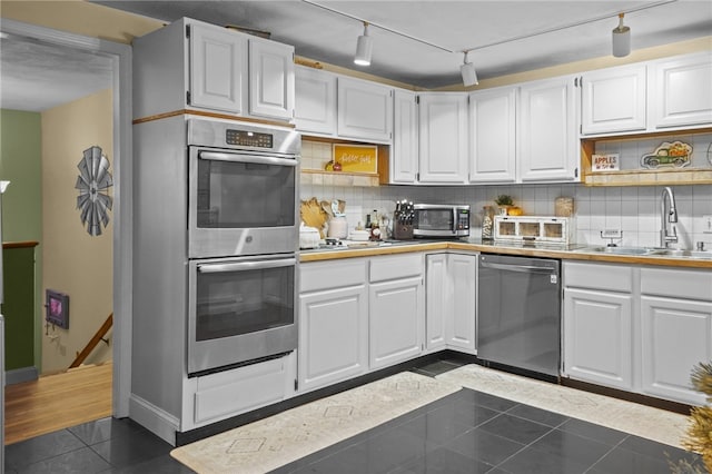 kitchen with appliances with stainless steel finishes, white cabinetry, sink, dark tile patterned flooring, and backsplash