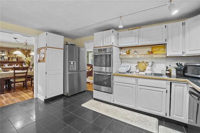 kitchen featuring appliances with stainless steel finishes, white cabinets, backsplash, and dark tile patterned flooring