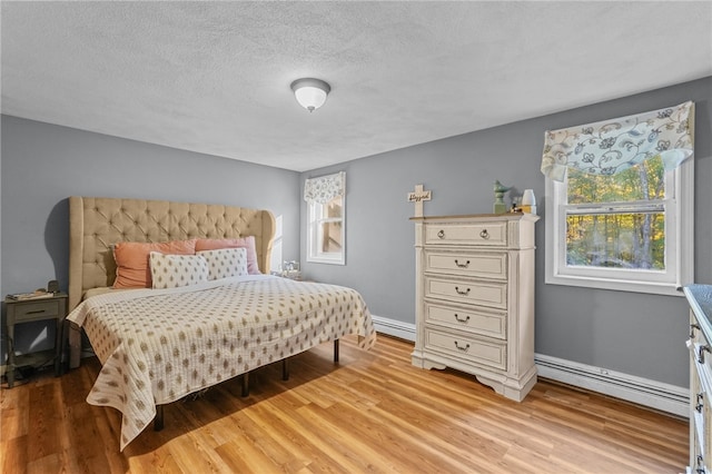 bedroom with baseboard heating, multiple windows, light hardwood / wood-style flooring, and a textured ceiling