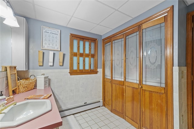 bathroom with tile patterned floors, a paneled ceiling, tile walls, baseboard heating, and vanity