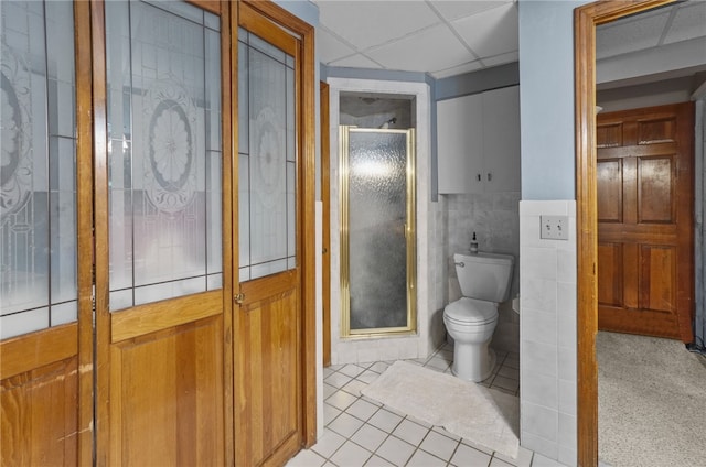 bathroom featuring tile patterned flooring, tile walls, a drop ceiling, a shower with shower door, and toilet