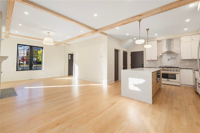 kitchen with white cabinets, high end stove, a center island, wall chimney exhaust hood, and decorative light fixtures