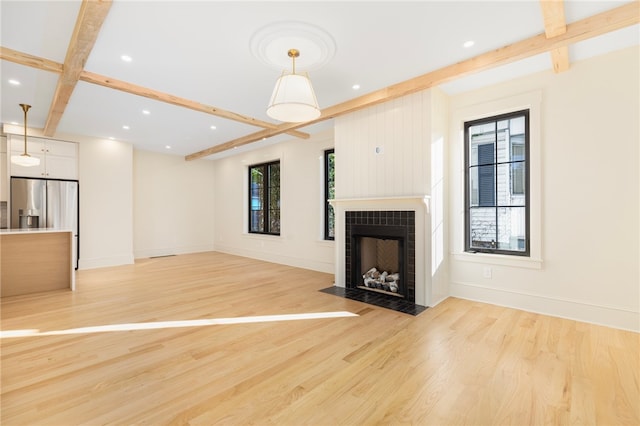 unfurnished living room with beamed ceiling, light hardwood / wood-style flooring, and a tiled fireplace