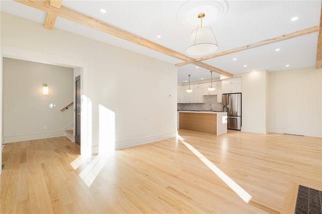 unfurnished living room featuring light hardwood / wood-style floors, beamed ceiling, and sink