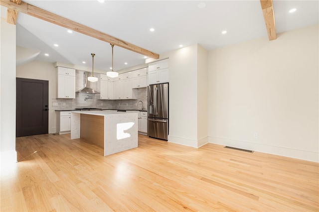 kitchen featuring wall chimney range hood, a center island, white cabinetry, appliances with stainless steel finishes, and light hardwood / wood-style floors