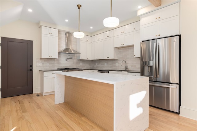 kitchen featuring wall chimney range hood, white cabinetry, light wood-type flooring, appliances with stainless steel finishes, and tasteful backsplash