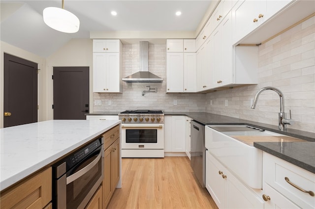 kitchen featuring wall chimney range hood, light stone countertops, decorative light fixtures, white cabinetry, and appliances with stainless steel finishes