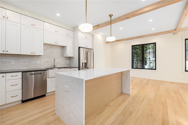 kitchen with appliances with stainless steel finishes, beam ceiling, pendant lighting, and a kitchen island