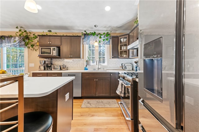 kitchen featuring exhaust hood, appliances with stainless steel finishes, light hardwood / wood-style flooring, crown molding, and sink