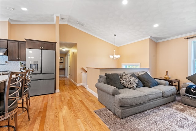 living room with crown molding, vaulted ceiling, a notable chandelier, and light hardwood / wood-style floors