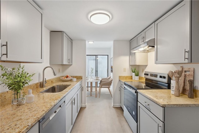 kitchen featuring light wood-style floors, under cabinet range hood, light stone counters, a sink, and appliances with stainless steel finishes