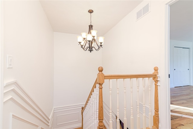 stairway with hardwood / wood-style floors and a notable chandelier