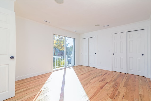 unfurnished bedroom with multiple closets, ornamental molding, light hardwood / wood-style flooring, and access to exterior