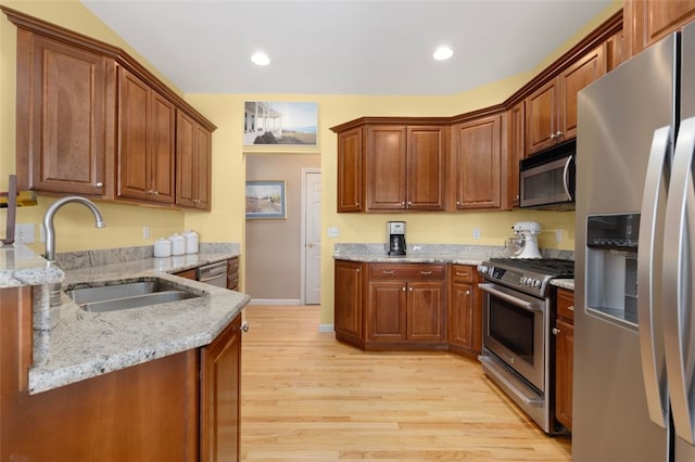 kitchen with appliances with stainless steel finishes, sink, light stone counters, and light hardwood / wood-style flooring